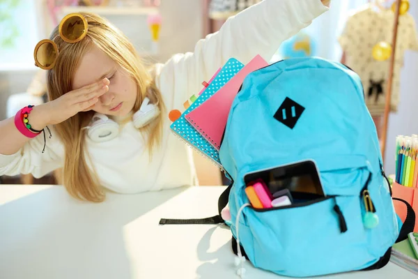 modern school girl with workbooks and blue backpack in white sweatshirt doing dabbing gesture at home in sunny day.
