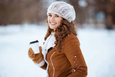 Orta yaşlı mutlu bir kadının portresi. Eldivenleri ve sıcak kakaolu örgü şapkası ve koyun derisi ceketiyle. Kışın şehir parkında..