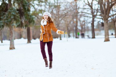 Eldivenli, örgü şapkalı ve koyun derisi ceketli, kışın şehir parkında neşeli gülümseyen orta yaşlı kadının tam boy portresi..