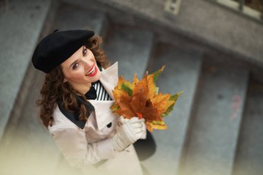 Merhaba Kasım ayı. Sonbahar sarısı yapraklı bej renkli trençkotlu mutlu orta yaşlı kadın manzarası sonbaharda şehir dışında..