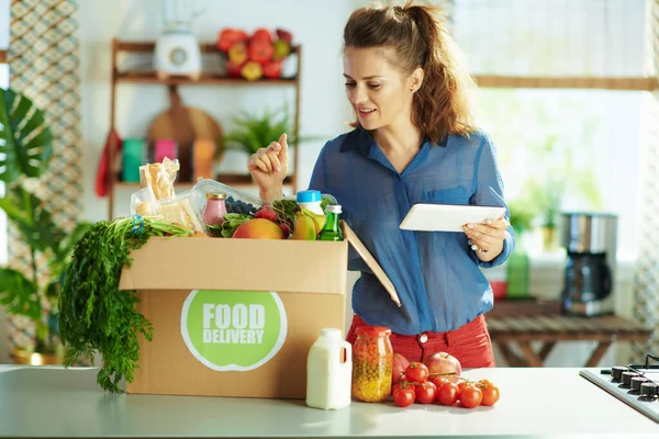 Food delivery. middle aged woman with food box using tablet PC app in the kitchen.