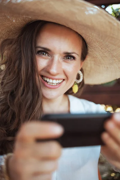 Beyaz Tişörtlü Şapkalı Gülümseyen Moda Kadınının Portresi Verandada Akıllı Telefon — Stok fotoğraf
