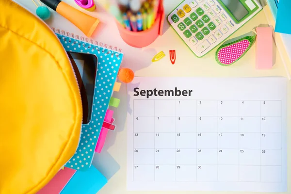 Back to school. Upper view of white table with workbooks, stationary, september calendar and backpack at school child room in sunny day.