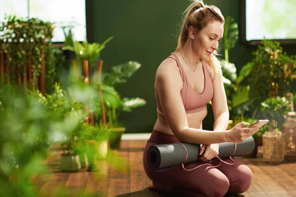 modern woman with yoga mat using smartphone at modern green home.