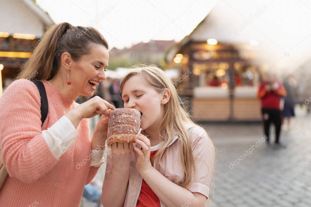 happy modern mother and daughter at the fair in the city eating trdelnik.
