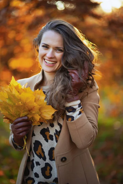 Hello september. happy young woman in beige coat with autumn yellow leaves outdoors on the city park in autumn.