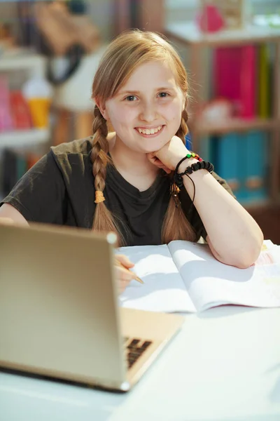 幸せな現代の生徒はノートパソコンとワークブックを持ってグレーのシャツで晴れた日に自宅でオンライン教育を受けています — ストック写真