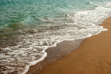 Yumuşak deniz dalgaları kumlu kıyılarda vuruyor.