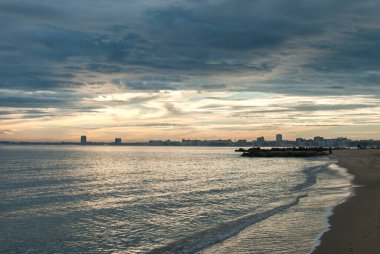 Kum sahili, rıhtım ve sakin deniz suları bulutlu günbatımında