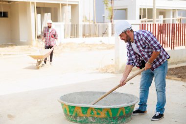 İnşaat işçisi koruyucu eldiven ve başlık takıyor inşaat alanında çimento karıştırıyor..