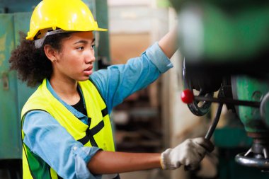Güvenlik gözlüğü takan kadın, parçaları delmek için makineyi kontrol ediyor. Metal torna fabrikası.