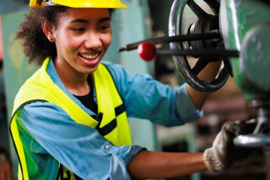 Güvenlik gözlüğü takan kadın, parçaları delmek için makineyi kontrol ediyor. Metal torna fabrikası.