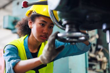 Güvenlik gözlüğü takan kadın, parçaları delmek için makineyi kontrol ediyor. Metal torna fabrikası.