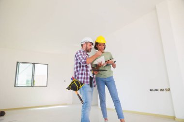 Kapalı alanda. Paten ve renk paletli bir ressam. Genç Afrikalı Amerikalı kadın ve İspanyol inşaat işçisi gülümseyen inşaatçılar