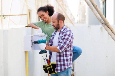 Açık havada çalışmak. Elinde bir aletle İspanyol erkek elektrik mühendisi yükleyici. Genç siyah kadın çift Bakım Hizmetleri Tamir ve Tamirat Konsepti