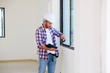 Yeni inşaat alanına pencere döşeyen bir adam. İspanyol inşaat işçisi eldiven ve başlık takıyor.