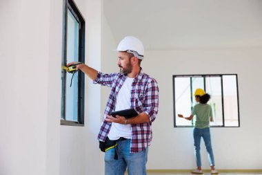 Yeni inşaat alanına pencere döşeyen bir adam. İspanyol inşaat işçisi eldiven ve başlık takıyor.