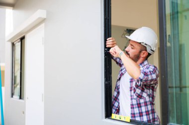 Man installing windows in  new house construction site. Hispanic Construction worker wearing protect gloves and hardhat helmet