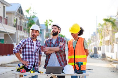 Takım dizüstü bilgisayarda çalışıyor. Profesyonel Makine Mühendisi Ekibi, inşaat sahasının altındaki imalat fabrikasında güvenlik kaskı takıyor..