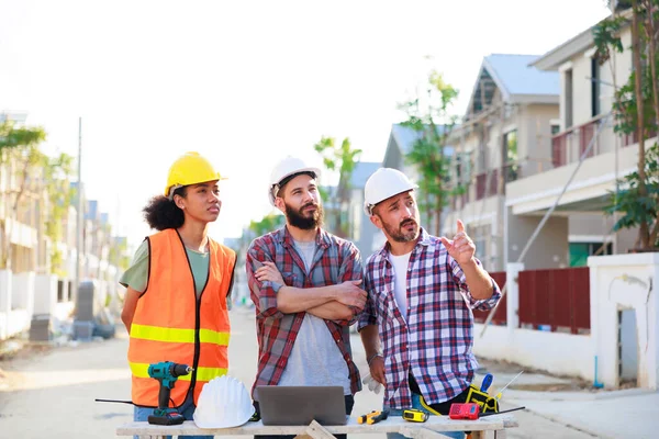 Takım dizüstü bilgisayarda çalışıyor. Profesyonel Makine Mühendisi Ekibi, inşaat sahasının altındaki imalat fabrikasında güvenlik kaskı takıyor..