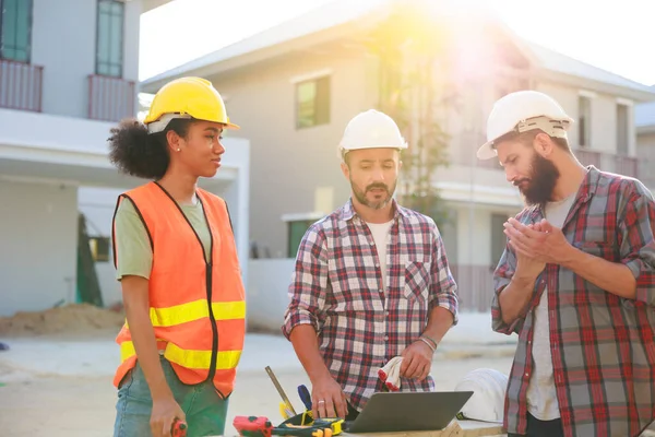 Takım dizüstü bilgisayarda çalışıyor. Profesyonel Makine Mühendisi Ekibi, inşaat sahasının altındaki imalat fabrikasında güvenlik kaskı takıyor..