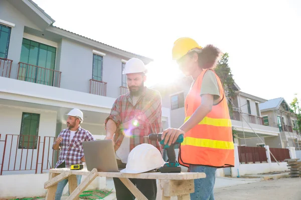 Takım dizüstü bilgisayarda çalışıyor. Profesyonel Makine Mühendisi Ekibi, inşaat sahasının altındaki imalat fabrikasında güvenlik kaskı takıyor..