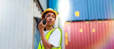 Black female dock worker control loading containers box from cargo at warehouse container yard. Marine and carrier insurance concept. cargo shipping container box in logistic shipping yard