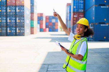 Black female dock worker control loading containers box from cargo at warehouse container yard. Marine and carrier insurance concept. logistic shipping yard