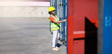 Zenci kadın tersane işçisi depo deposundaki kargodan gelen konteynırları açıyor. Denizci ve uçak sigortası konsepti. lojistik nakliye deposu