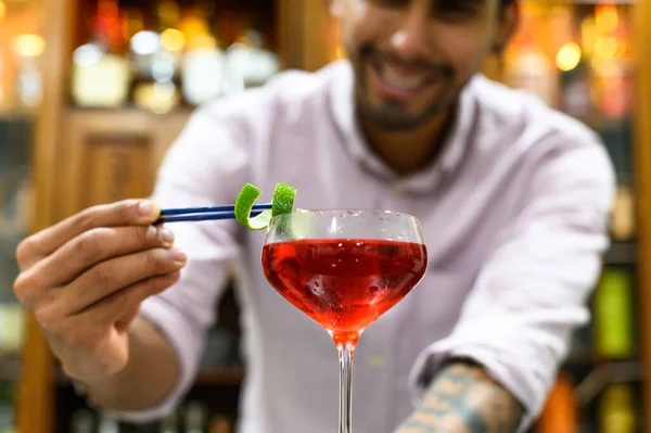Close-up van glas met rode drank die barman nauwkeurig versieren met sinaasappelschil. — Stockfoto