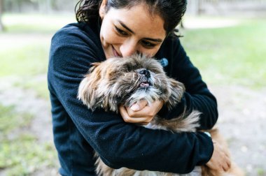 Cute young woman is kissing and hugging her little puppy. Love between owner and dog. Outdoor photo in the park, selective focus. Lifestyle concept.