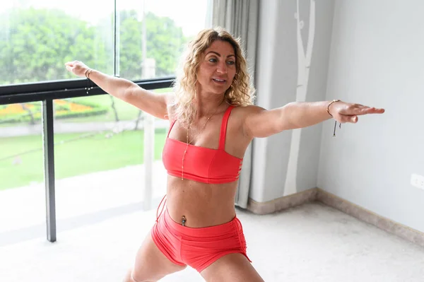 Молодая женщина делает упражнения баланса и растяжения спорта йоги, красные леггинсы спортивной одежды и сверху, яркая комната дома утром. Лицензионные Стоковые Фото