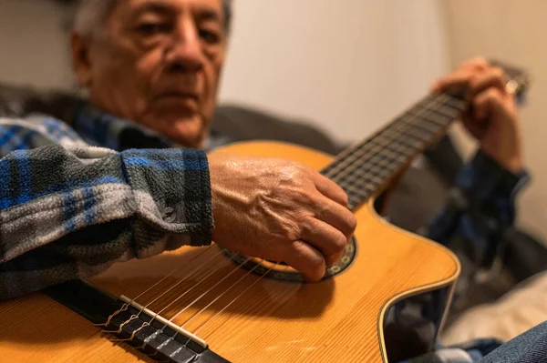 Viejo tocando la guitarra acústica y sentado en el sofá. Imagen De Stock