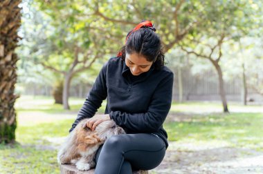 Şirin genç bayan küçük köpeğine sarılıyor. Sahibi ve köpeği arasındaki aşk. Parktaki açık hava fotoğrafı, seçici odaklanma. Yaşam tarzı kavramı