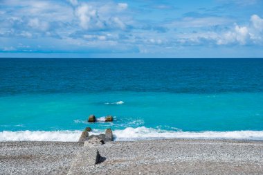 Deniz dalgalarının altında eski bir rıhtım. Mavi gökyüzü, mavi deniz ve kıyı şeridi. Deniz kıyısında eski bir bina.