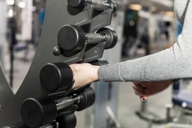 Kız, dambılları dikey raftan depolamak için alıyor. Sınıflar salonda, arka plan bulanık.