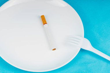 Tabakta yemek yerine çatal ve sigara, arka plan mavi. Sigara yemek yerine sigara içmek daha iyi, sigara içmek daha iyi.