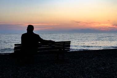 Gün batımında deniz kıyısında oturan bir adamın silueti. Denizde yalnızlık, huzur içinde yat.