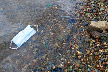Virüsler için bir yüz maskesi rezervuarın kıyısında bulunur. Su ve maske. Hijyen ürünleri dağıtımı sorunları