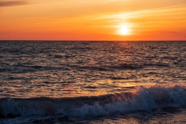 Denizde dalgalar, gün batımında gökyüzü. Bulutlar akşam gökyüzünü kapladı. Gökyüzünde güzel bulutlar denizin üzerinde