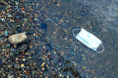 Baraj gölünün kıyısında tek kullanımlık bir yüz maskesi var. Kayalık kıyı ve maske. bir salgın sırasında yeni atık