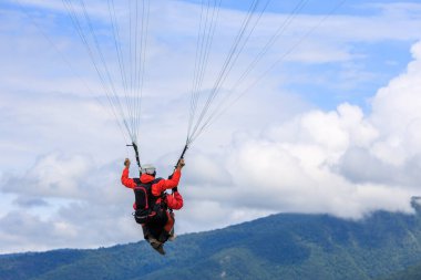 Dağların ve gökyüzünün arka planında yamaç paraşütü yapan eğitmen ve turist sineği kablolara tutunuyor. duygusal rahatlama