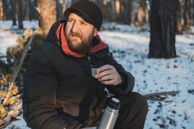 Kış ormanında elinde termosla sakallı bir adam. Kışın gezgin istirahati