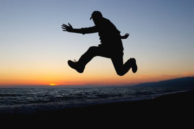 Zıplayan bir adam gün batımında deniz kıyısında yere değmez. Deniz kenarında bir akşam, rahatlamanın sevinci