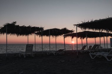 Sahildeki eşyaların siluetleri, boş bir sahilde güneşlenme yatağı ve şezlonglar. Dün gün batımında deniz sahilinde gezginler yoktu.