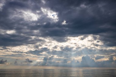 Denizin üzerindeki bulutlu gökyüzü, bulutların arasından geçen güneş ışınları. Sonbahar günü deniz manzarası