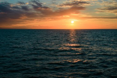 Gün batımında deniz manzarası, ufuk çizgisi ve batan güneş. Su yüzeyinde güneşten gelen patika
