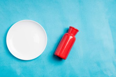 Kırmızı vazo ve mavi arka planda boş beyaz tabak. yuvarlak beyaz tabak ve kırmızı vazo, farklı renkte.