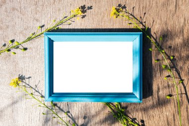 Ahşap bir yüzeyde mavi ahşap çerçeve, çerçevenin etrafında sarı çiçekler. Çerçevedeki bir yazı için boş alan