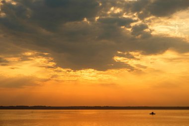 Gün batımında gölde tekne silueti. Güneşten gelen ışınlar bir bulut ve yazın bir su kütlesi.